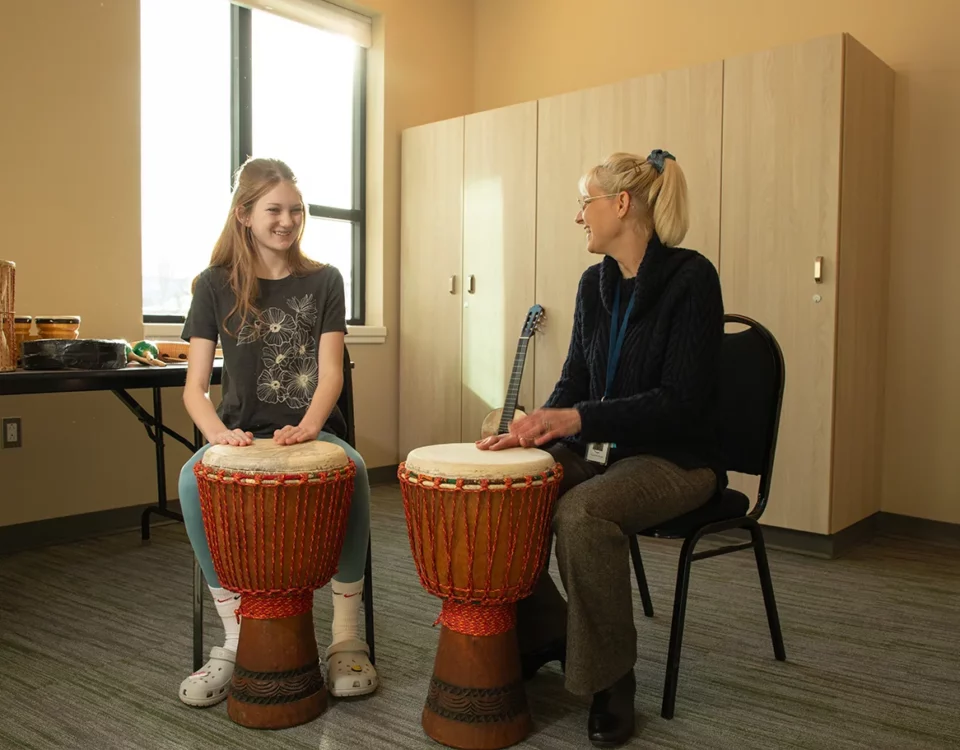 A teacher and student sit at drums in a music therapy session
